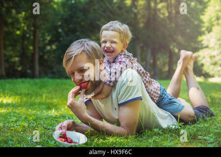 Junger Vater und sein Sohn Essen Erdbeeren im Park. Picknick. Outdoor portrait Stockfoto