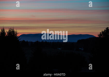 Die Sonne geht hinter Ben Wyvis in den schottischen Highlands, in der Nähe von Inverness am ersten Tag der Britische Sommerzeit und einen anderen Tag der herrlichen Sonnenschein und blauem Himmel in den Highlands. Stockfoto