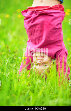 Glückliche kleine Mädchen stehen auf dem Kopf stehend auf dem Rasen im Sommerpark Stockfoto