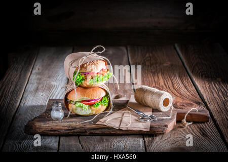 Frische Burger zum Mitnehmen verpackt in Papier auf alten Holztisch Stockfoto