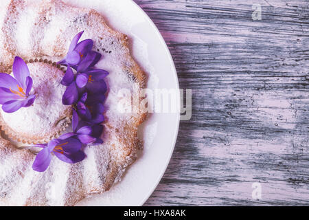 Kuchen auf weißen Teller dekoriert mit Krokus Blume auf hölzernen hellen schönen Hintergrund. Frühling. Ansicht von oben. Textfreiraum Stockfoto