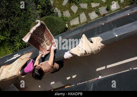 AJAXNETPHOTO. LOUVECIENNES, FRANKREICH. -HÄUSLICHE SZENE-FRAU SCHÜTTELN TEPPICH VOM BALKON DES WOHN-HOCHHAUS. FOTO: JONATHAN EASTLAND/AJAX REF: FX112103 5145 Stockfoto