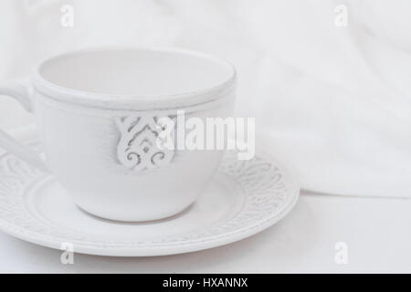 Weißes Relief Keramik Teetasse mit Untertasse auf Holztisch Baumwollstoff, Reinheit Konzept, minimalistische, gestylte Bild für social-Media, Banner, header Stockfoto