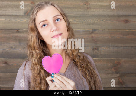 Junge Frau mit lustigen rosa Herz in der hand, hölzernen Hintergrund. Spaß Foto Requisiten und Zubehör für Shootings Stockfoto