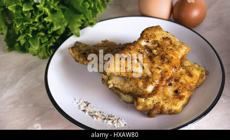 Fisch paniert in Ei und Mehl auf einem weißen Teller mit Salat und Salz und Kräutern der Provence Stockfoto