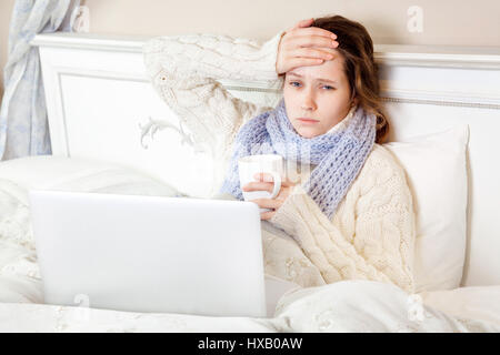 Kranke Frau schlecht fühlen, ruhen und arbeiten mit ihrem Laptop und Internet in ihrem Bett zu Hause. Stockfoto