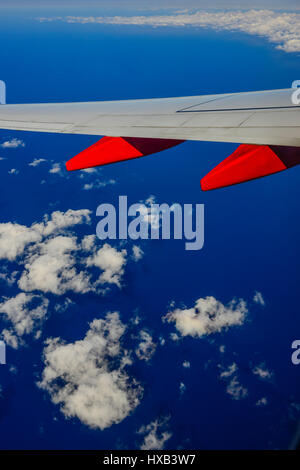 Eine Tragfläche im Vordergrund mit weißen Wolken und blauer Himmel gesehen vom Fenster des kommerziellen airliner Stockfoto