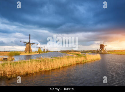 Erstaunliche Windmühlen. Rustikale Landschaft mit traditionellen holländischen Windmühlen in der Nähe von Wasserkanälen und blauen Wolkenhimmel und gelben Sonnenlicht. Farbenprächtigen Sonnenuntergang in Stockfoto