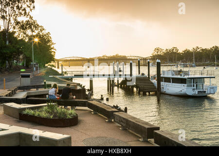 Paar entspannend mit Burnett-Brücke über dem Fluss entlang.  Bundaberg, Queensland, Australien Stockfoto