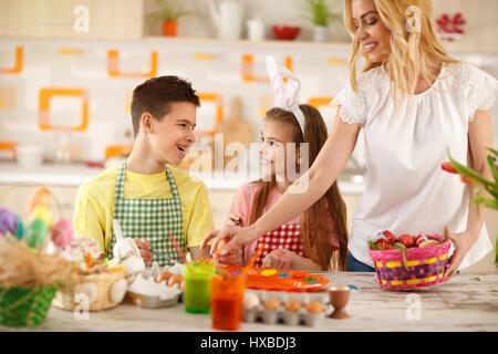 Mutter mit Kindern setzen bunte Ostereier im Korb Stockfoto