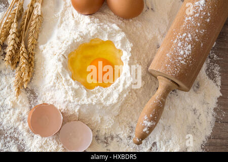 Grundzutaten für das backen - Teig, Mehl, Eiern und Nudelholz auf einem Holztisch Stockfoto