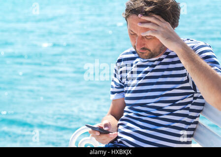 Männliche Touristen in abgespeckte Shirt mit Handy für die Kommunikation am Meer im Sommer Urlaub Urlaub Stockfoto