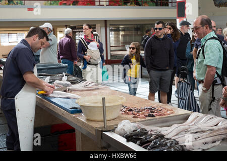 Touristen sehen einen Fischhändler, bereiten Sie ein Schwarzer Degenfisch in Filets zum Verkauf auf dem Fischmarkt in Funchal, Madeira Stockfoto