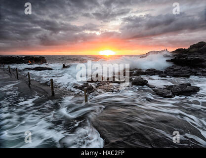 Schwere See mit großen Wellen und einem rosa Himmel bei Sonnenaufgang über Kiama Felsenpool, Kiama, Illawarra Coast, New-South.Wales, NSW, Australien Stockfoto