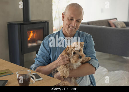 Lächelnder Mann Petting Hund vor Holz Ofen Kamin Stockfoto