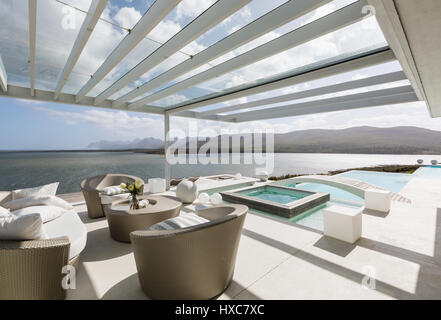 Sonnige moderne Luxus-Terrasse mit Infinity-Pool und das Meer sehen Stockfoto