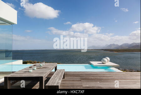 Sonnige ruhige moderne Luxus-Terrasse mit Infinity-Pool und das Meer sehen Stockfoto