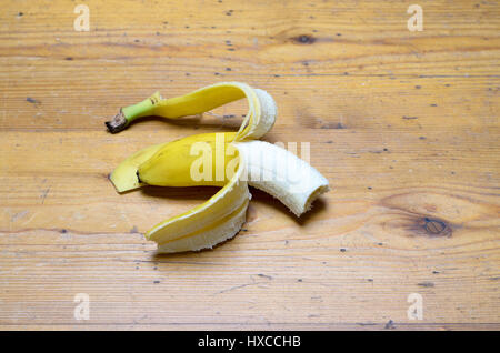 Teilweise geschälte Hälfte gegessen Reife gelbe Banane nach einem leckeren, gesunden Snack liegend in der Mitte ein Holztisch mit Textfreiraum, erhöhte Ansicht Stockfoto