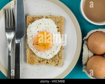 Flach Zusammensetzung und engen Ernte von einem pochierten Ei auf Toast, Sunny Side Up, Frühstück mit einer Tasse Tee oder Kaffee und Zwei rohe Eier in der Schale Stockfoto