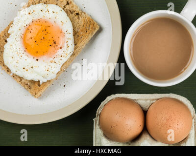 Flach Zusammensetzung und engen Ernte von einem pochierten Ei auf Toast, Sunny Side Up, Frühstück mit einer Tasse Tee oder Kaffee und Zwei rohe Eier in der Schale Stockfoto