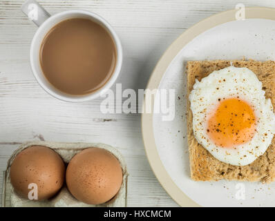 Flach Zusammensetzung und engen Ernte von einem pochierten Ei auf Toast, Sunny Side Up, Frühstück mit einer Tasse Tee oder Kaffee und Zwei rohe Eier in der Schale Stockfoto