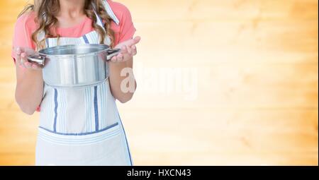 Digital Composite Frau in Schürze mit Pan gegen verschwommen gelbe Holzplatte Stockfoto