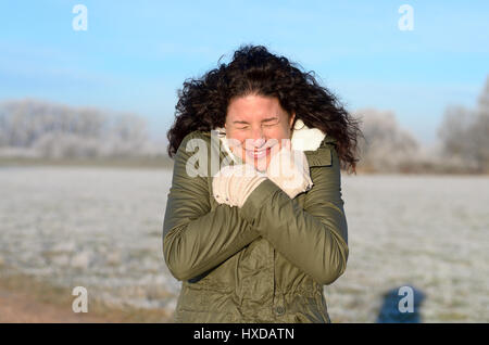 Attraktive junge Frau, die zitternd an einem kalten Wintermorgen mit Raureif aus den Bereichen wie sie einen erfrischenden Spaziergang entlang einer Landstraße genießt Stockfoto