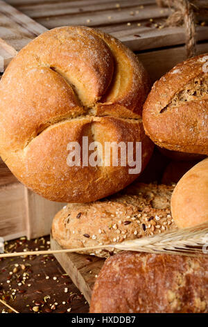 Nahaufnahme einer Auswahl an verschiedenen Brötchen und einige Ähren auf einem rustikalen Holztisch Stockfoto