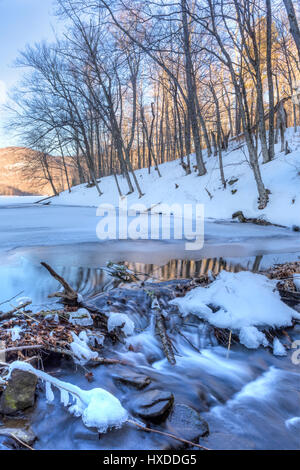 Reflexionen und Wellen im Wasser, das fließt aus teilweise gefrorenen großen Teich in den Catskills Mountains von New York. Stockfoto