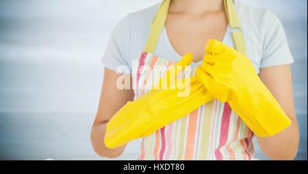 Digital Composite Frau in Schürze mit gelben Handschuhen gegen unscharfen grauen Holzplatte Stockfoto
