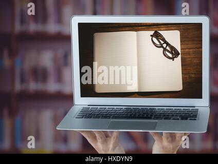 Digital Composite Hände mit Laptop zeigt offenes Buch und Brille gegen verschwommen Bücherregal mit lila-overlay Stockfoto