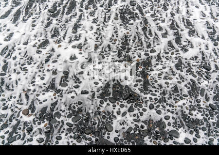 Meereswellen treten entlang der Brandung an einem schwarzen Sandstrand in Island Stockfoto