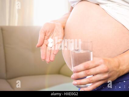 Digital Composite schwangeren Frau Mittelteil mit Medikamenten in unscharfen Wohnzimmer Stockfoto