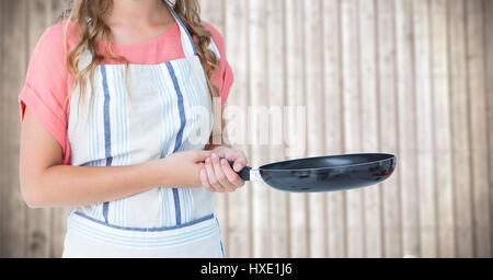 Digital Composite Frau in Schürze mit Bratpfanne gegen verschwommen Holzplatte Stockfoto