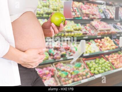 Digital Composite schwangeren Frau Mittelteil hält Apfel in unscharfen Gemüse Gang Stockfoto