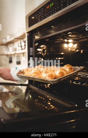 Zugeschnittenes Bild des Mannes herausnehmen Tablett mit frisch gebackenen Croissants aus dem Ofen in Kaffee chop Stockfoto