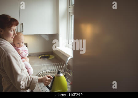 Mutter mit Baby während der Kaffeezubereitung in der heimischen Küche Stockfoto