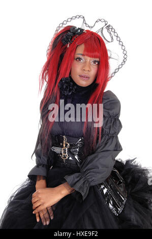 Eine schöne afroamerikanische Frau mit langen roten Haaren und einer Spitzen-Krone sitzt in einem schwarzen viktorianischen Kleid für weißen Hintergrund isoliert. Stockfoto