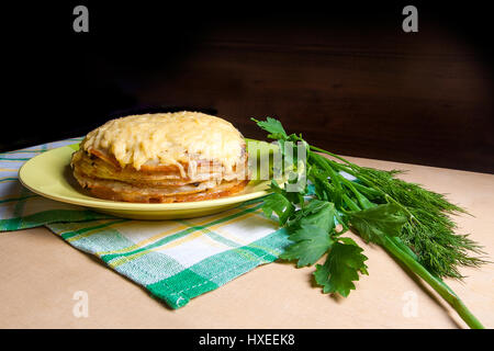 Pfannkuchen Sie-Torte mit Champignons und Hühnerfleisch, überbacken mit Käse auf grüne Platte. Pfannkuchen-Kuchen auf Teller mit Kräutern grün: grüne Zwiebel, Dill, Petersilie Arou Stockfoto