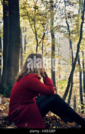 Junge Frau sitzt allein im Wald Stockfoto
