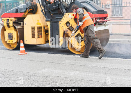 Bauarbeiter mit Schaufel. Städtische Straße im Bau, Asphaltierung im Gange. Stockfoto