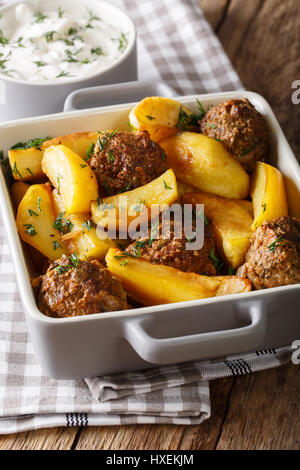 Frikadellen mit Kartoffel wedges in einer Petrischale für Backen und Sauerrahm close-up auf einem Tisch. Vertikal Stockfoto