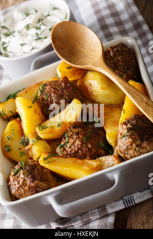 Frikadellen mit Kartoffeln in eine Auflaufform Gericht und Sauerrahm Nahaufnahme auf einem Tisch. Vertikal Stockfoto