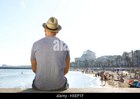 Porträt von hinten ein Mann sitzt allein auf der Suche am Strand im Sommer Stockfoto