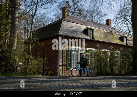 Ein kleiner Junge Zyklen den Wildhüter Haus am Eingang der Privatbesitz de Merode Burg, vorbei am 25. März in Everberg, Belgien. Die Wildhüter Haus liegt neben dem Fürsten Kopfsteinpflaster (Prinsendreef) in Everberg und wurde um 1770 erbaut. Das Haus war vertrauter als die neue Herberge (Nieuwe Herbergh). Dieses Haus wurde vermietet. Kunsthistoriker bezeichnete es als ein Haus aus dem 18. Jahrhundert im provenzalischen regency Stil. Am Ende des 19. Jahrhunderts wurde das Haus den Wildhüter Haus de Merode Burg. Letzteres ist der Besitzer des Hauses sowie. Die Wildhüter Haus kennt man in Stockfoto