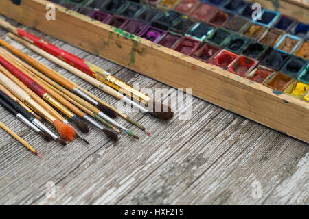 Box mit Wasserfarben und Pinsel auf Holzuntergrund Stockfoto