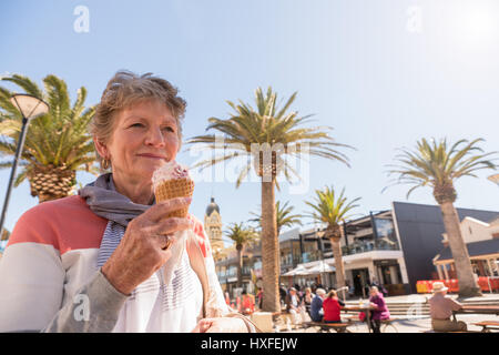 Glücklich lächelnde Dame, Essen ein Eis am Strand Glenelg, Adelaide, South Australia Stockfoto