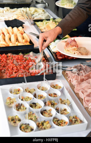 Menschen helfen sich auf Nahrung auf einem Buffet mit Fleisch, Gemüse und Salate in einer Kantine oder bei einem Catering Event hautnah auf seine Hand in eine Gastronomie Konzeptionierung Stockfoto