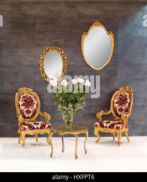 Elegante retro oder Vintage Stil Inneneinrichtung mit zwei hölzernen Polstersessel rund um einen kleinen Couchtisch mit Blumen und zwei verzierten spiegeln auf Stockfoto