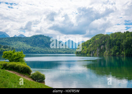 See Alpsee, in der Nähe von Hohenschwangau Schloss in Bayern Staates mit der umgebenden Naturlandschaft und Berge, Deutschland, unter bewölktem Himmel blau Stockfoto